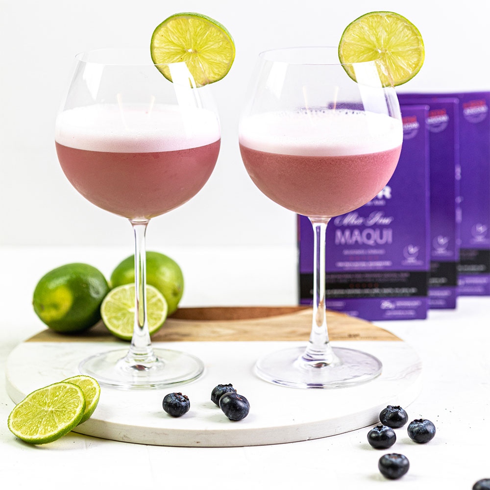 Dos cócteles preparados con Our Sour Maqui, decorados con limón, acompañados de limones y arándanos frescos